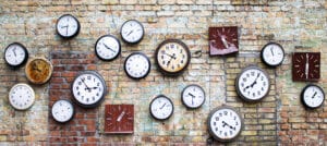 A brick wall full of analog clock faces of various styles.