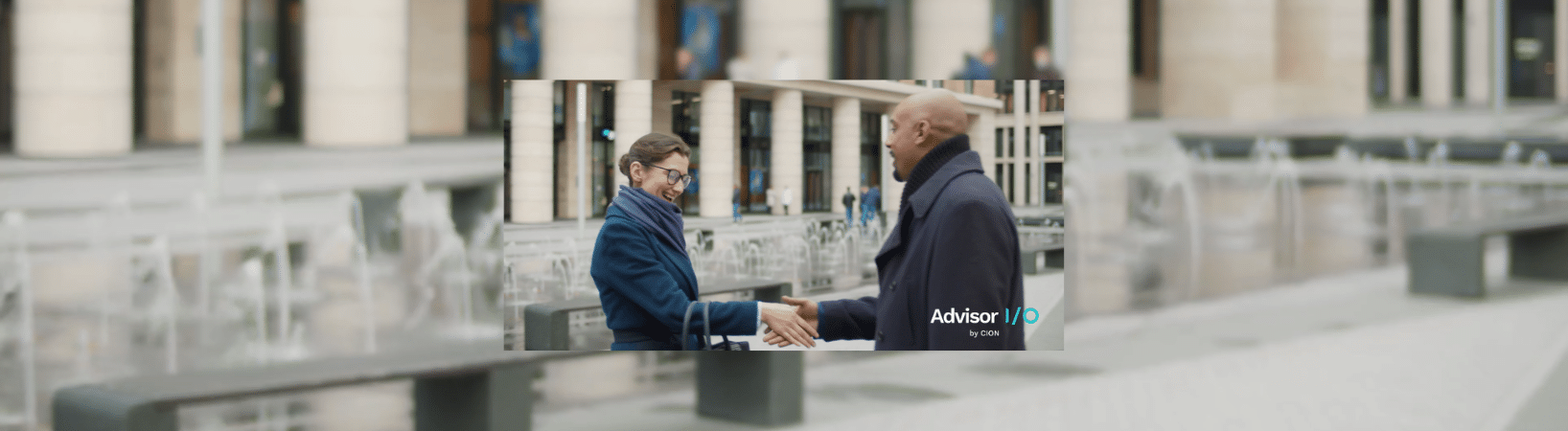 A man and a woman shake hands outdoors in front of a building.