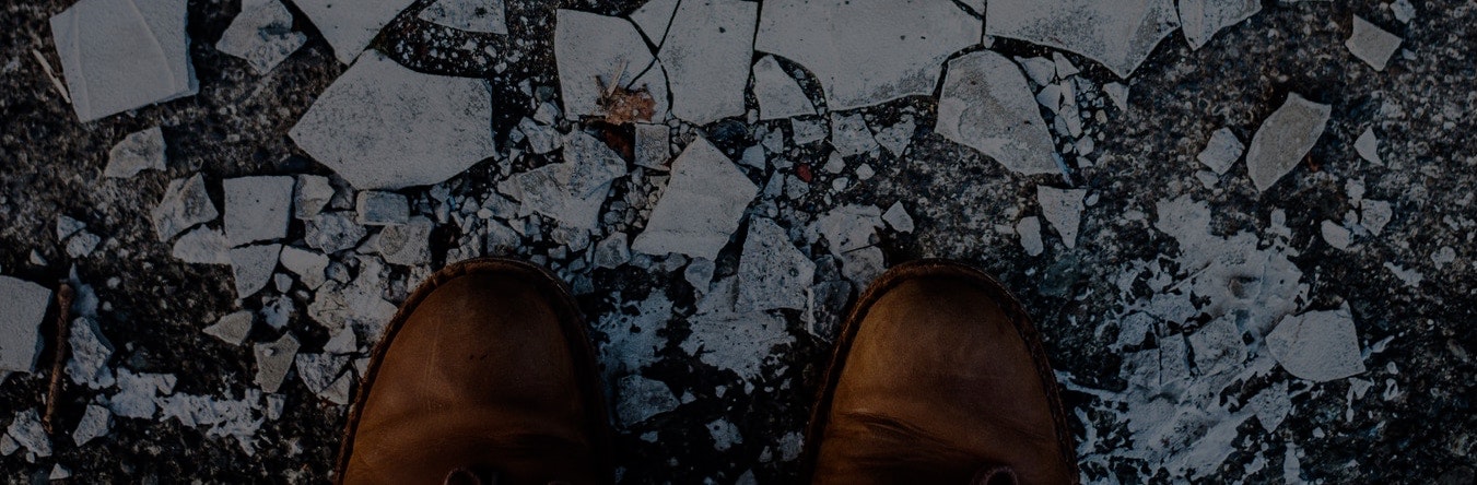 Top-down view of brown shoes next to crushed pieces of ceramic on the ground.